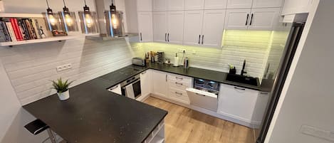A modern kitchen with white cabinets, a black countertop, and a built-in dishwasher.