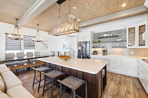 A modern kitchen with a large island, wooden bar stools, and a hanging light fixture.
