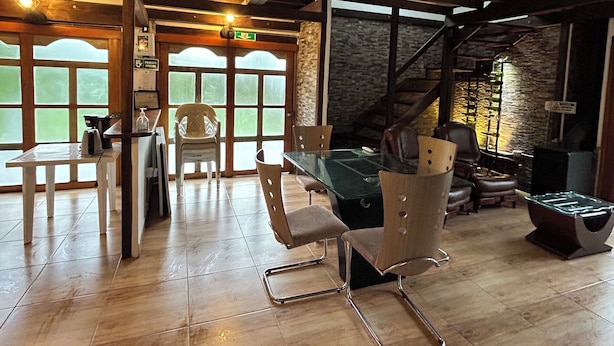 A spacious room with a wooden floor, a glass-top table, and several chairs. There is a stone wall and a staircase in the background. - Casa Campestre Forest House - Unique Relaxation in Salento, Quindío (Salento)