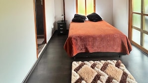 A bedroom with a wooden ceiling, a bed with a red cover, two black pillows, a nightstand, a lamp, and a window with blinds. - Casa Campestre Forest House - Unique Relaxation in Salento, Quindío (Salento)