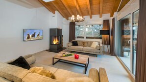 Un salon moderne avec une cheminée, un ensemble de canapés, une table basse et une grande fenêtre avec des rideaux.