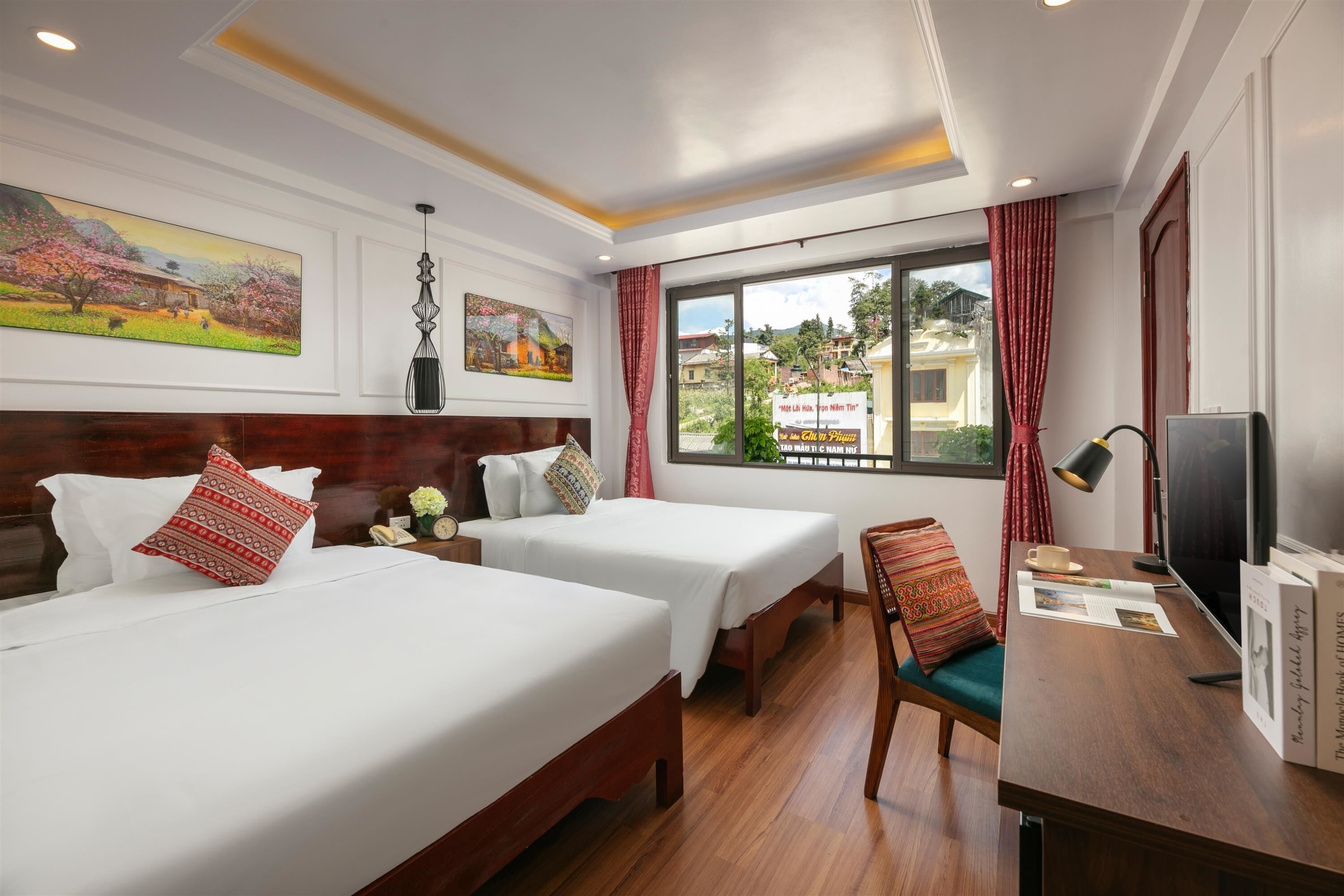 A hotel room with two beds, a desk with a chair, a TV, and a window with a view of the outside.