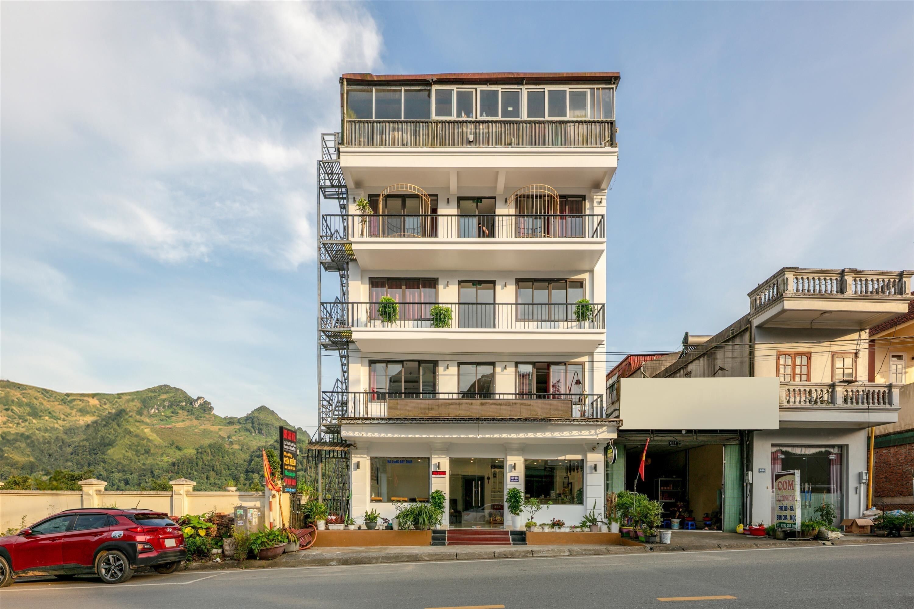 Un edificio a più piani con balconi, un negozio al piano terra e un'auto rossa parcheggiata davanti.
