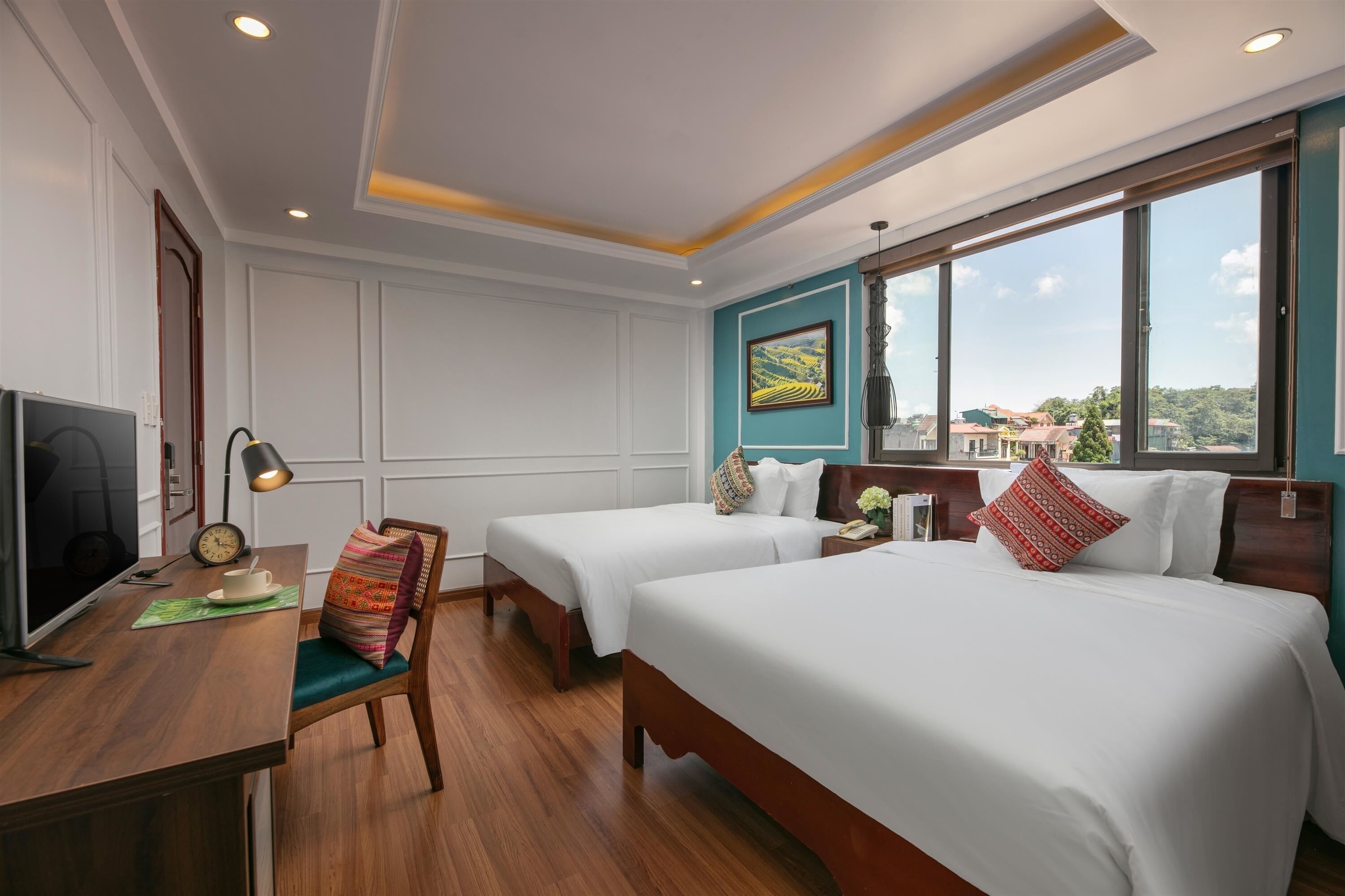 Habitación de hotel con dos camas, un escritorio con computadora, una silla y un amplio ventanal con vista a la ciudad.