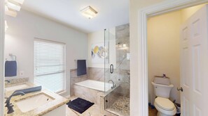 A modern bathroom with a glass-enclosed shower, a bathtub, and a toilet.