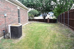 A backyard with a brick house, a wooden fence, and a large tree.