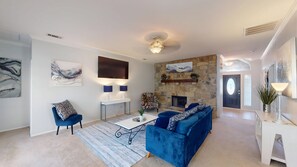 A modern living room with a blue sofa, a coffee table, and a stone fireplace. - FL001 | Flower Mound Home | 3BD | Yard | Workspace (Flower Mound)