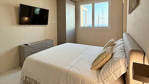 A bedroom with a bed, a TV, a dresser, and a window.