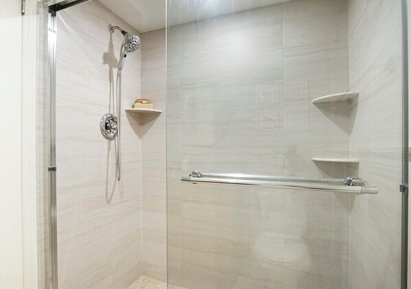 Uma área de chuveiro moderna com porta de vidro, chuveiro manual e duas barras para toalhas.