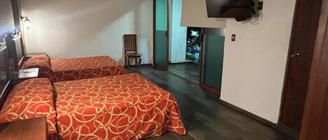 Habitación de hotel con dos camas, un televisor montado en la pared, una silla y una puerta que da a un balcón.