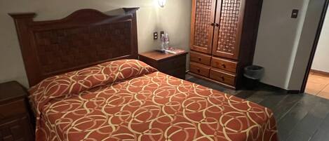 A neatly made bed with a patterned bedspread, a wooden nightstand with a lamp, and a wardrobe with a traditional design.