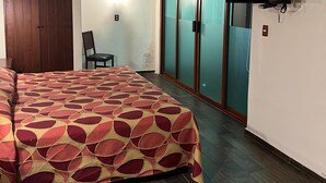 A bedroom with a bed, a television mounted on the wall, a wardrobe, and a chair.