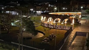 A well-lit outdoor area with a circular seating arrangement, a small pool, and a pathway leading to a building with arched entrances.