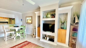 Un espacio habitable compacto con zona de comedor, televisor integrado y estantes decorativos.