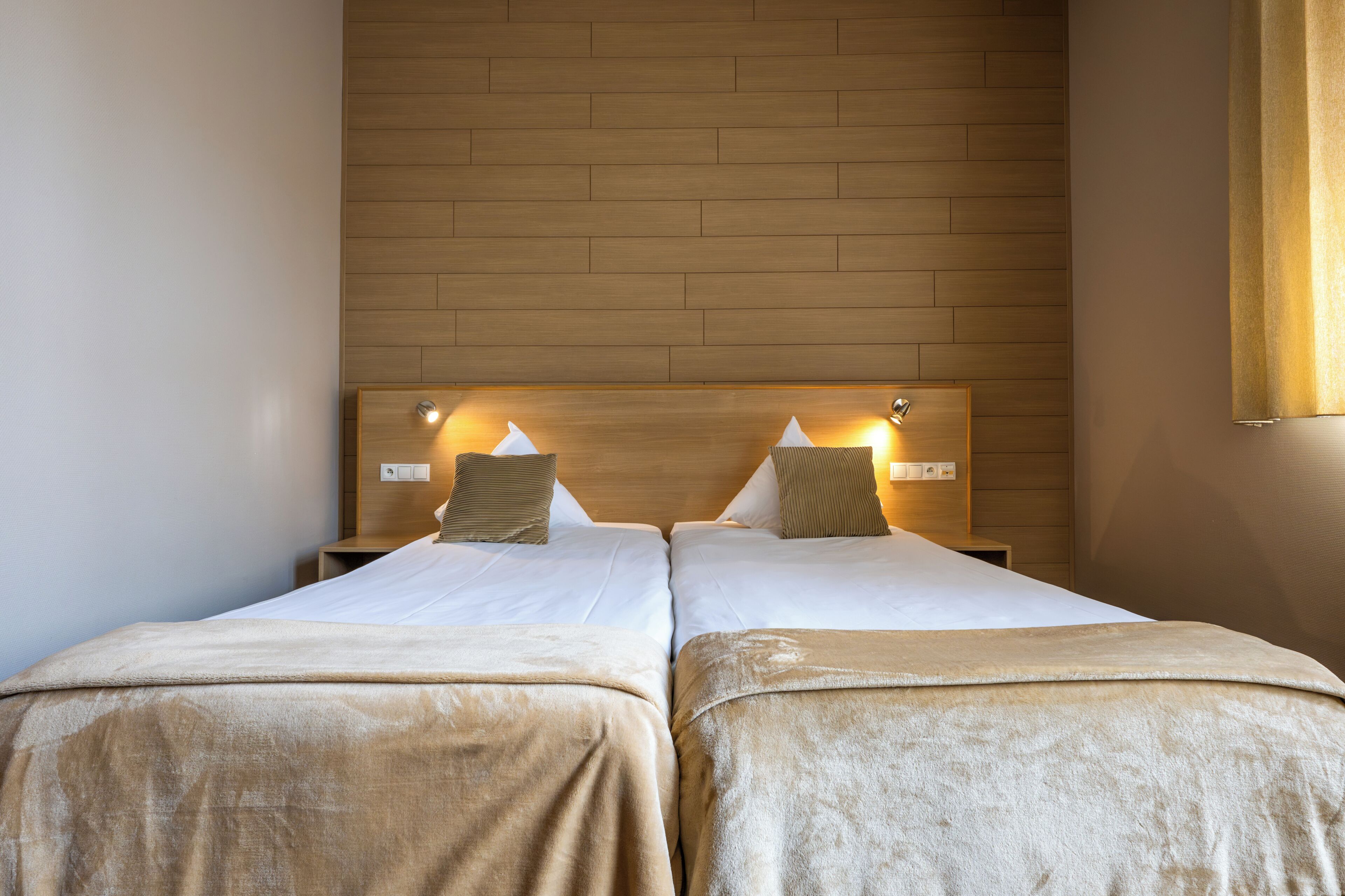 A double room with two beds, each with a headboard, a bedside table, and a lamp.