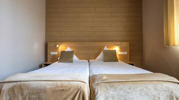 A double room with two beds, each with a headboard, a bedside table, and a lamp.