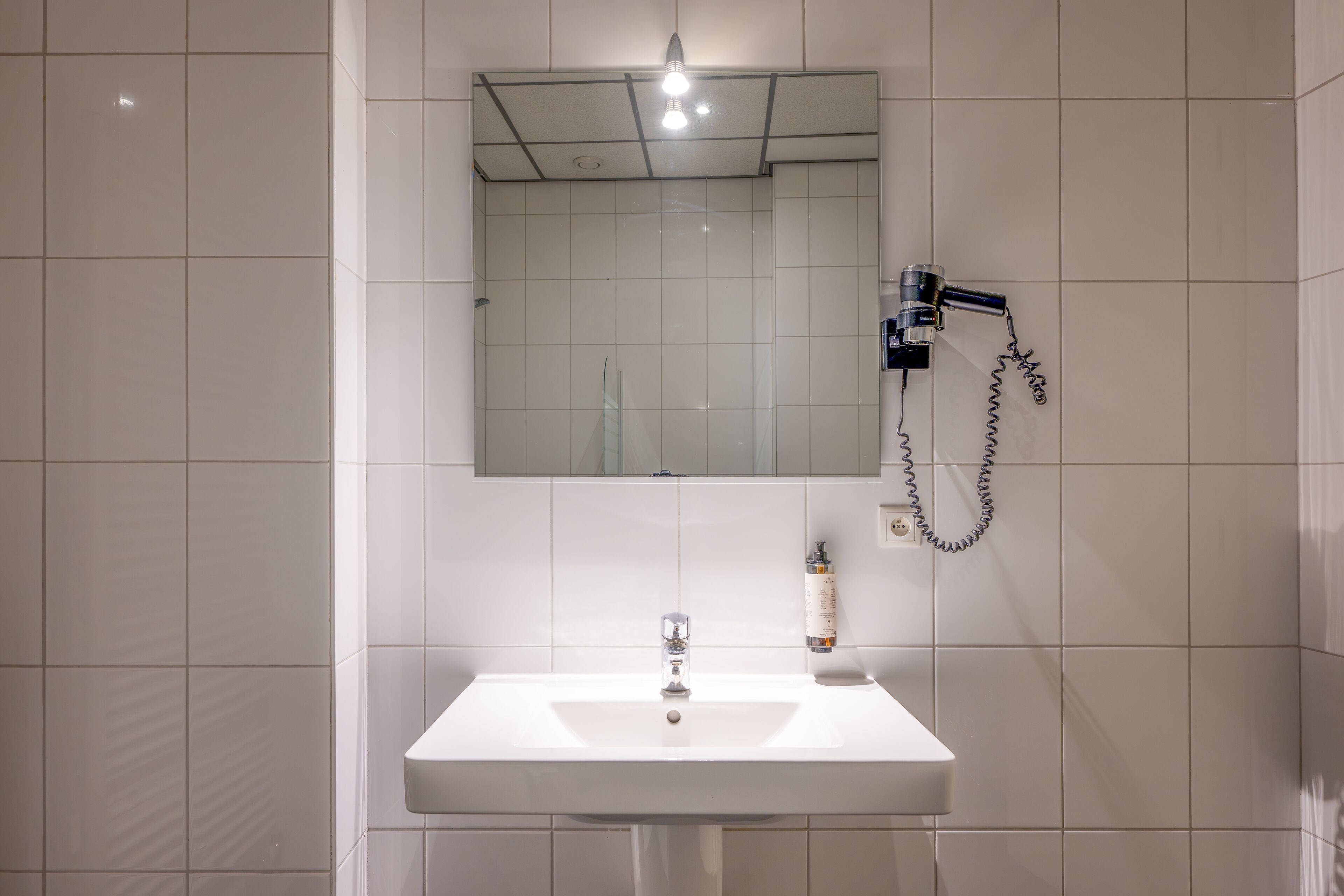 A bathroom with a white sink, a mirror, and a hairdryer mounted on the wall.