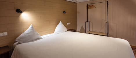 A hotel room with a large bed, two pillows, a wooden headboard, a wall-mounted light, and a wardrobe with a mirror.