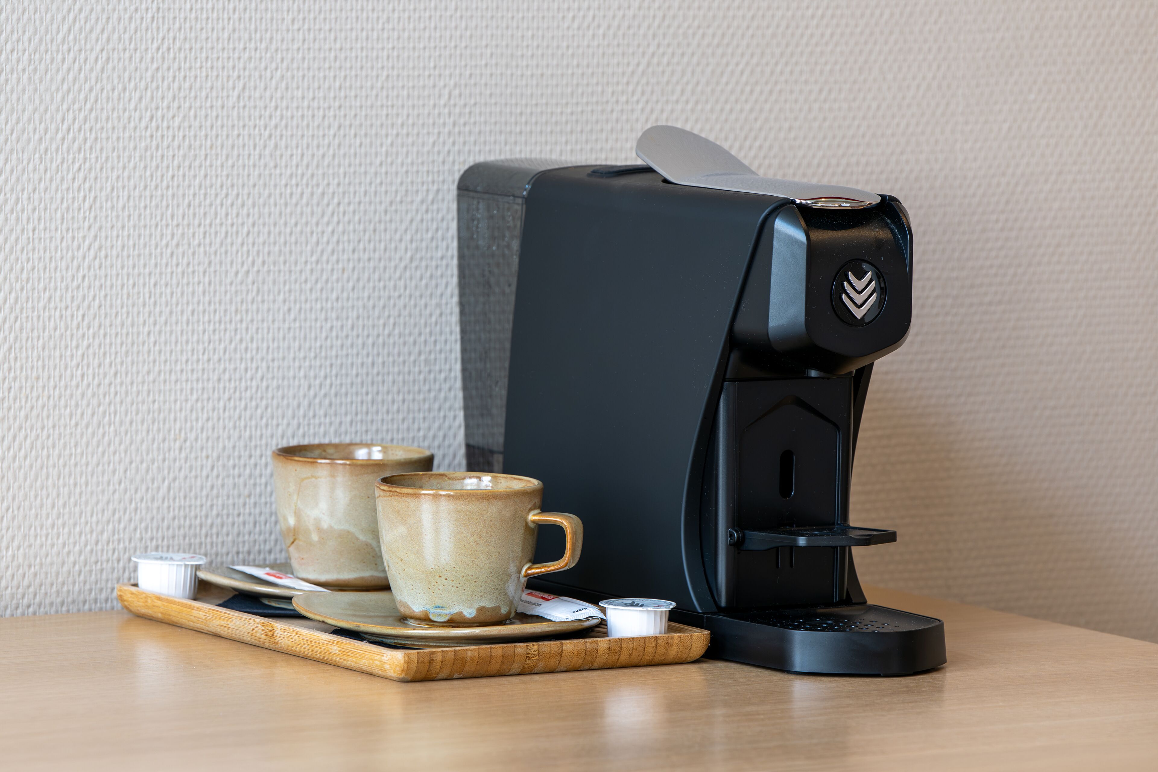 A coffee machine with two ceramic cups on a wooden tray.