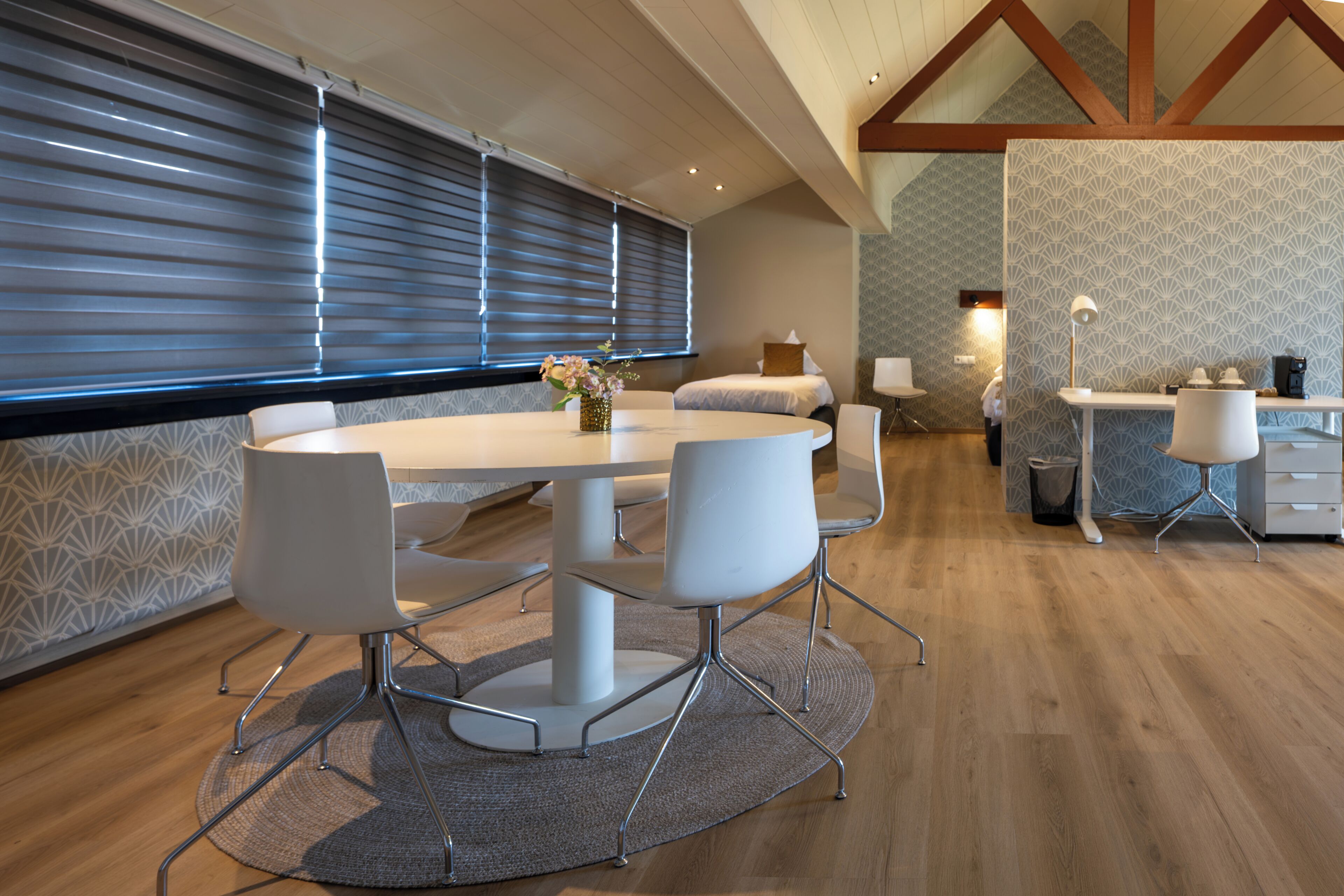 Een moderne eethoek met een ronde tafel, witte stoelen en een bloevas.