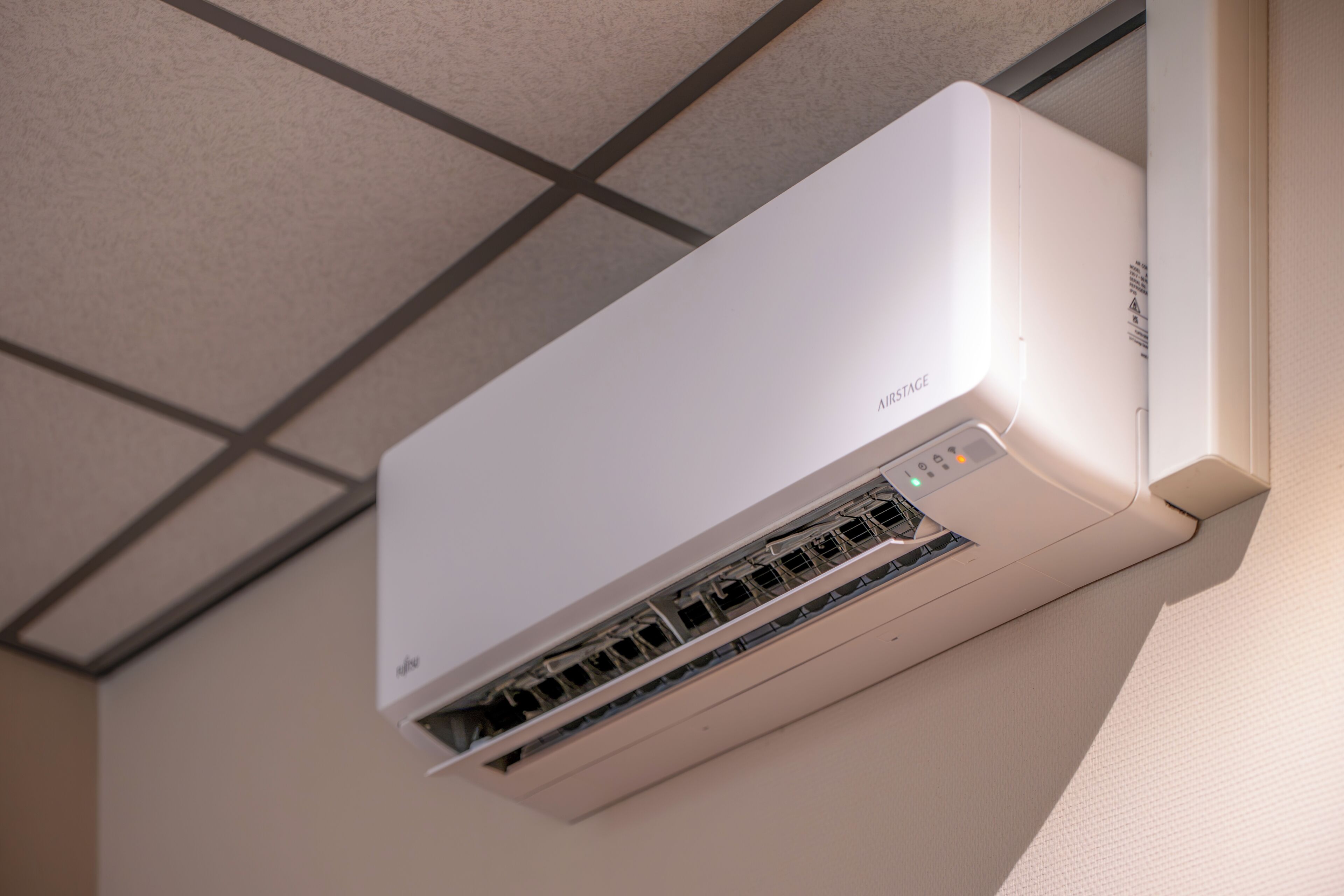 Eine weiße Klimaanlage an der Wand montiert, mit sichtbarer Bedieneinheit und Lüftungsgittern.