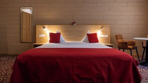 A hotel room with a large bed, two bedside tables, a mirror, a small table with chairs, and a patterned carpet.