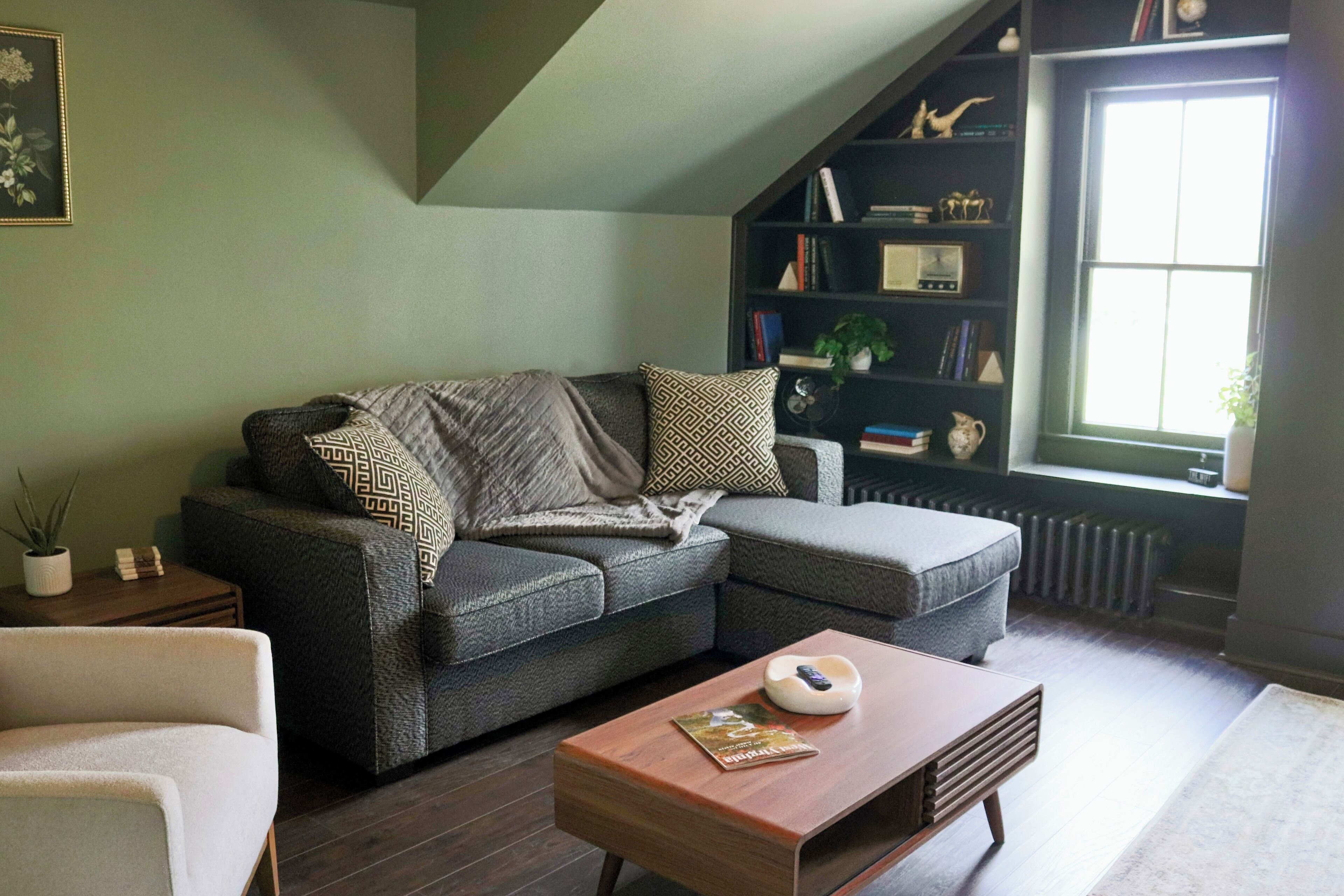 En moderne stue med en hjørnesofa, et tr æbord og en reol fyldt med bøger og pynteting.