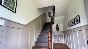 Eine Holztreppe mit Handlauf, weißer Wandverkleidung und einem Heizkörper im Hintergrund.