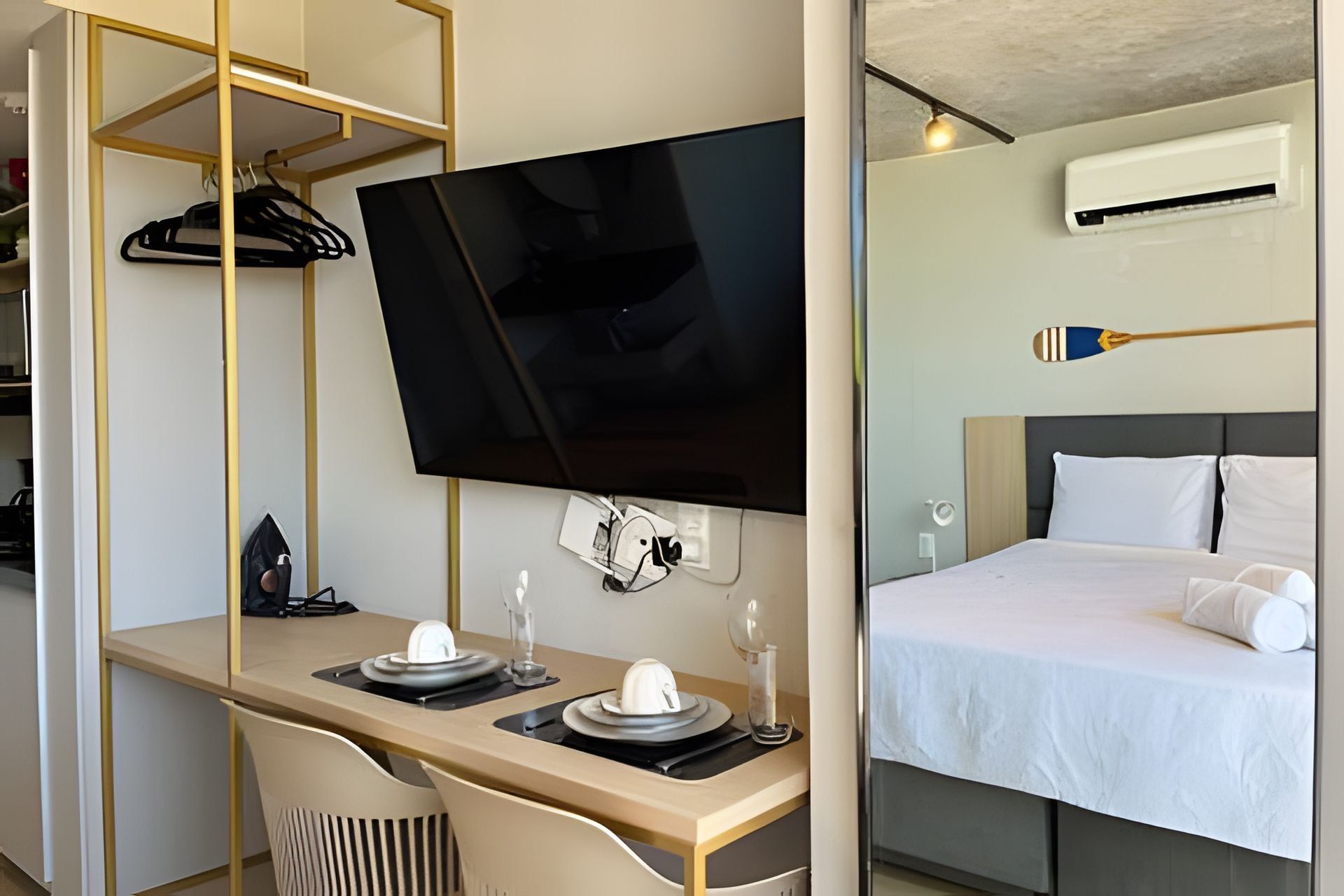 A hotel room with a bed, a desk with a TV, a coat rack, and an air conditioning unit.