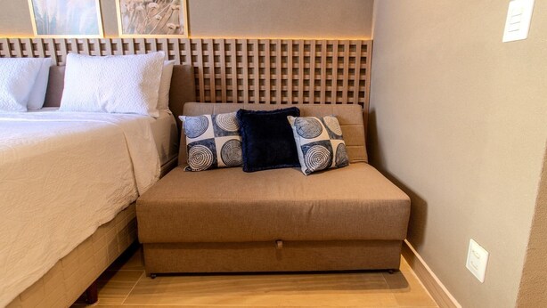 A bedroom with a bed, a sofa, and two wall-mounted light switches. - Setai Yach (Joao Pessoa)