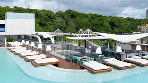 A poolside area with lounge chairs, umbrellas, and a glass railing overlooking a body of water. - Setai Yach (Joao Pessoa)