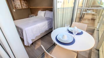 Habitación de hotel con cama, una mesa de comedor con sillas y vistas a través de un ventanal.