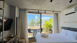 A hotel room with a bed, a desk with a computer, a TV, a balcony with a view of palm trees, and a ceiling with recessed lighting. - Setai Yach (Joao Pessoa)