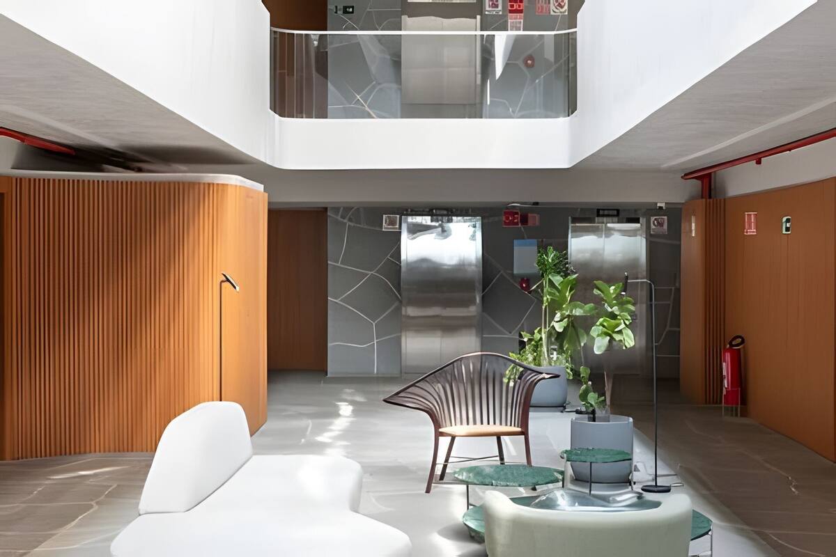 A modern lobby with a white sofa, a wooden panel wall, a glass elevator, and a potted plant.