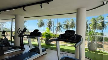 Un gimnasio con cintas de correr y equipo de ejercicio, ventanas amplias y vistas a palmeras.