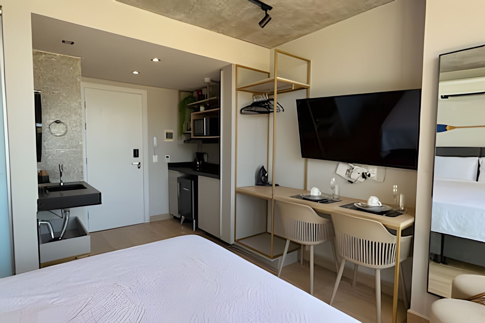 Una habitación de hotel moderna con una cama, un escritorio con dos sillas, un televisor y una kitchenette.