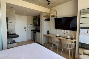 A modern hotel room with a bed, a desk with two chairs, a television, and a kitchenette. - Setai Yach (Joao Pessoa)