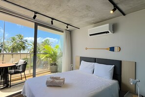 A hotel room with a bed, a potted plant, a dining area with chairs, and a view of palm trees. - Setai Yach (Joao Pessoa)