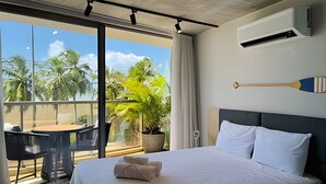 A hotel room with a bed, a potted plant, a table with chairs, and a balcony with a view of palm trees. - Setai Yach (Joao Pessoa)