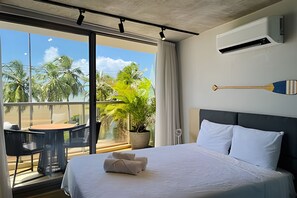A hotel room with a bed, a potted plant, a table with chairs, and a balcony with a view of palm trees. - Setai Yach (Joao Pessoa)