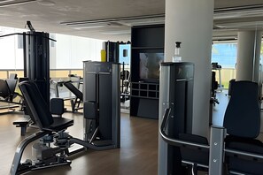 A gym with various exercise machines, large windows, and a view of the outside. - Setai Yach (Joao Pessoa)