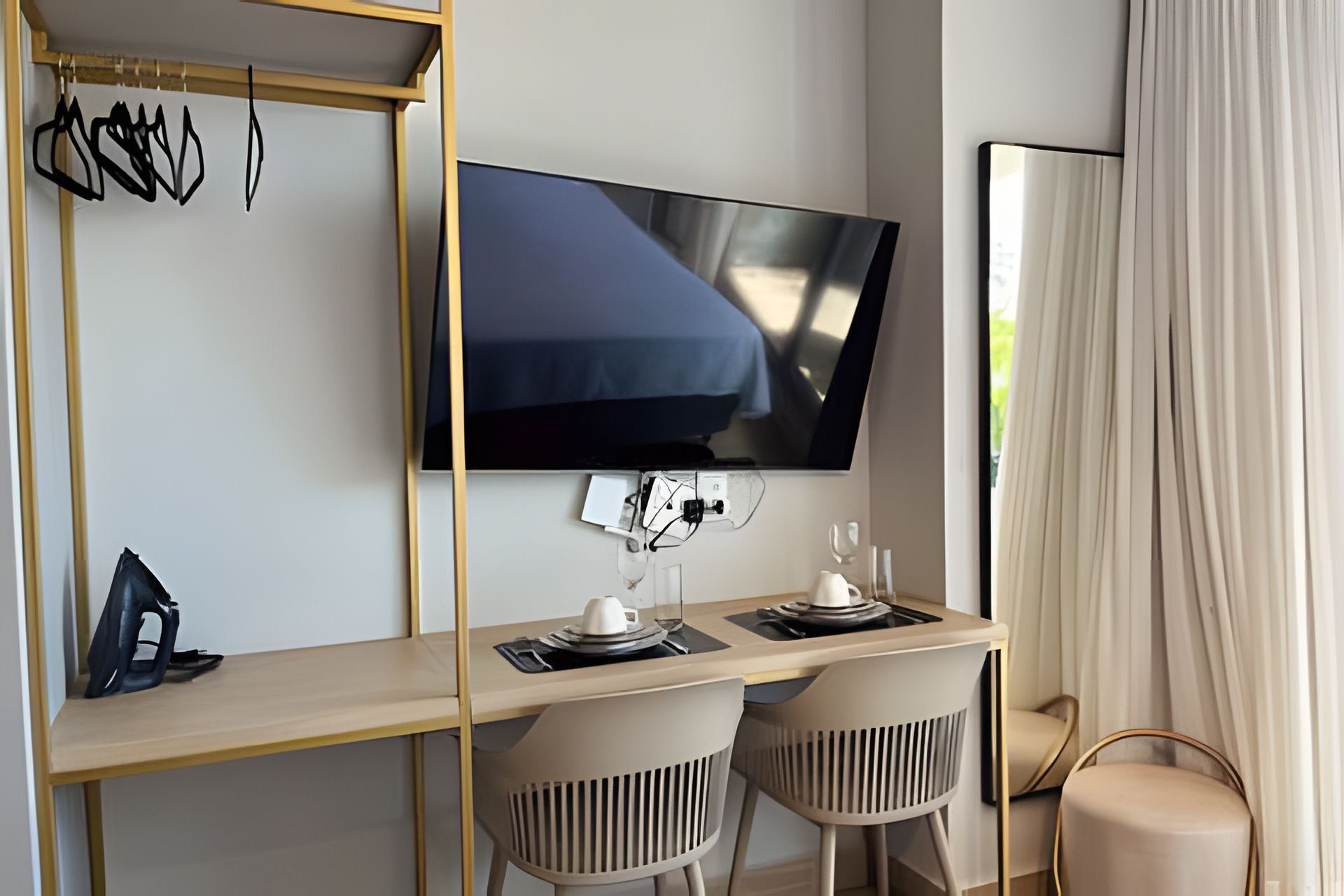 A hotel room with a desk, two chairs, a television, a mirror, and a window with curtains.