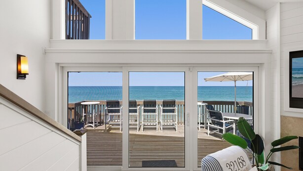 A view from a balcony overlooking the ocean, with a deck chair area and a large umbrella.