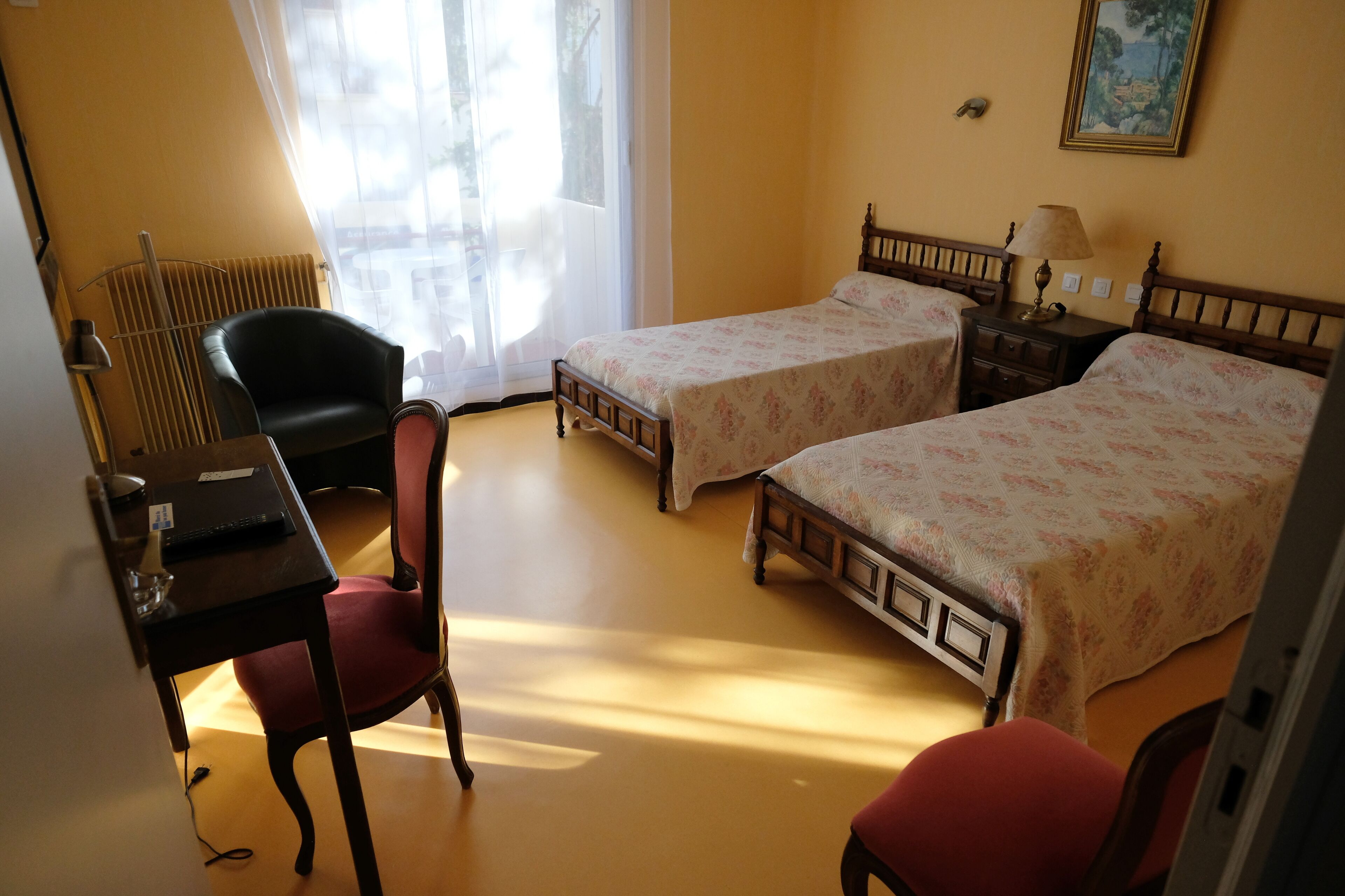 A room with two beds, a desk, a chair, and a radiator.