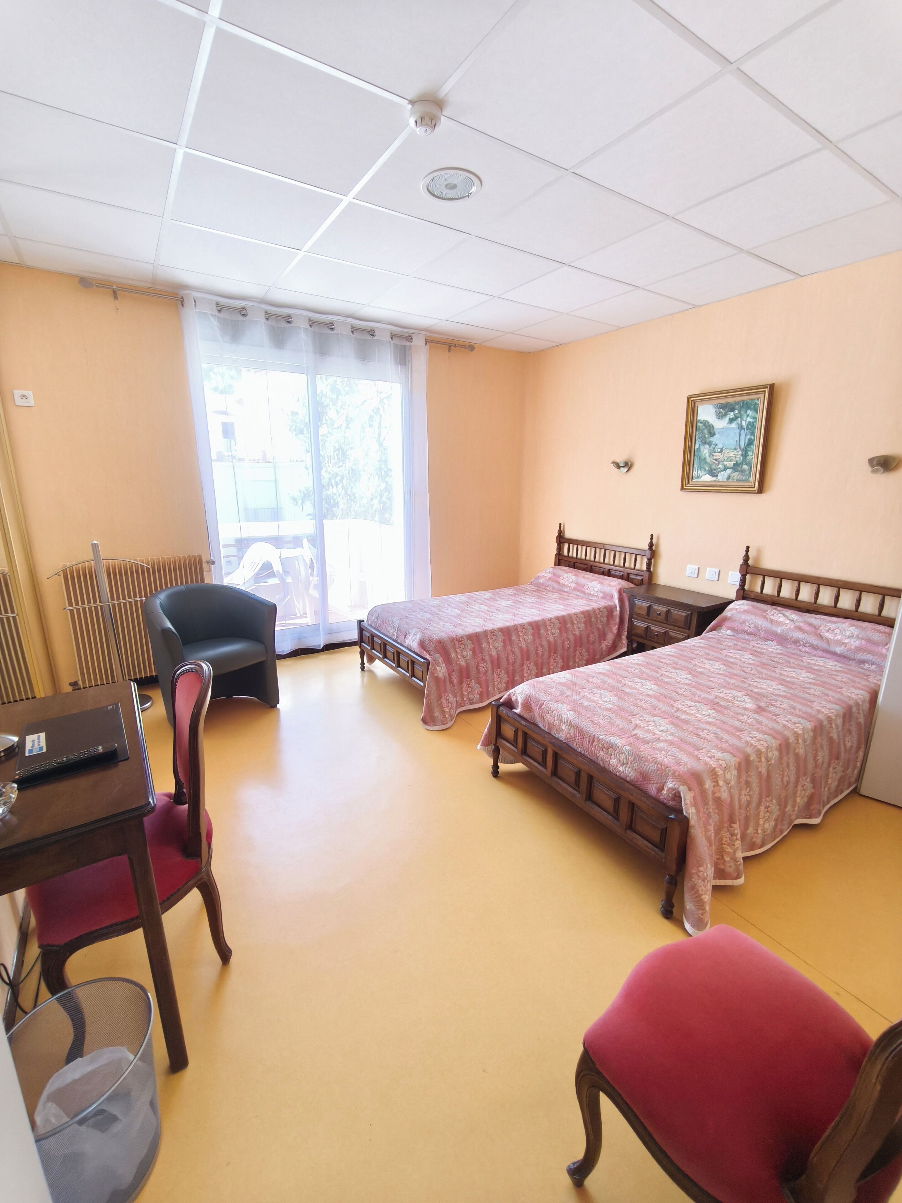 Una habitación con dos camas de madera, un escritorio con una computadora portátil, una silla, un radiador y una ventana con cortinas.