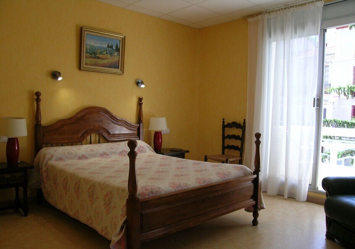 Une chambre à coucher avec un lit en bois, deux lampes de chevet, une table de nuit, une chaise et une fenêtre avec des rideaux.