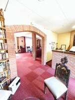 Um hall amplo com carpete vermelho, arco de tijolos, balcão de recepção e uma cadeira de madeira.