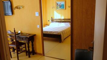 A hotel room with a wooden desk, a chair, a bed, and a mirror reflecting the room.