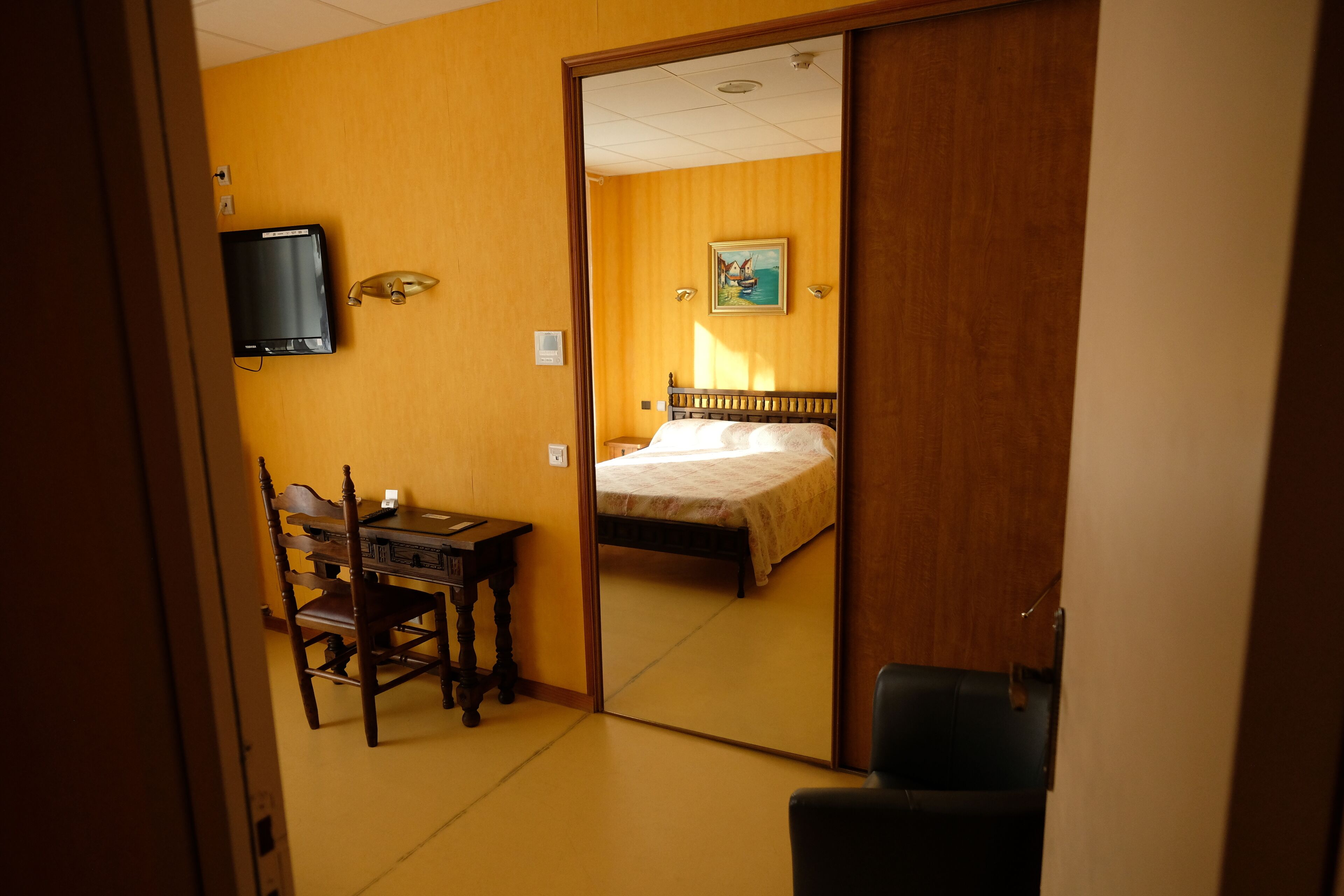 Ein Hotelzimmer mit einem Bett, einem Schreibtisch mit Stuhl, einem Fernseher an der Wand und einem Bild.