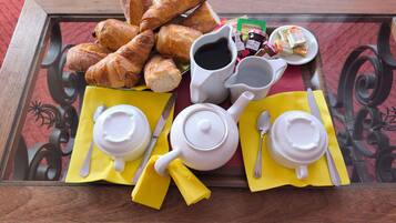 A breakfast tray with croissants, jam, butter, and coffee on a glass table.